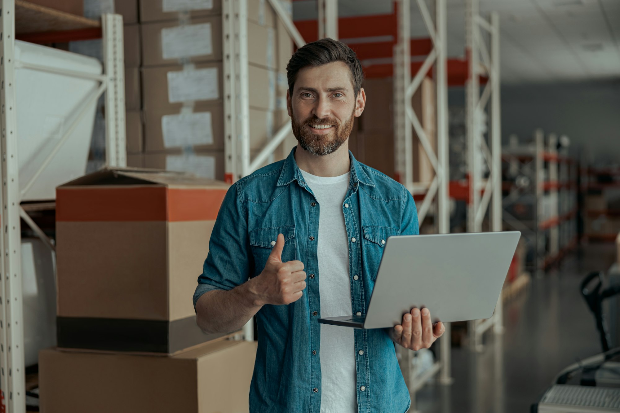 Warehouse worker standing with laptop on manufacturing and raise his finger up